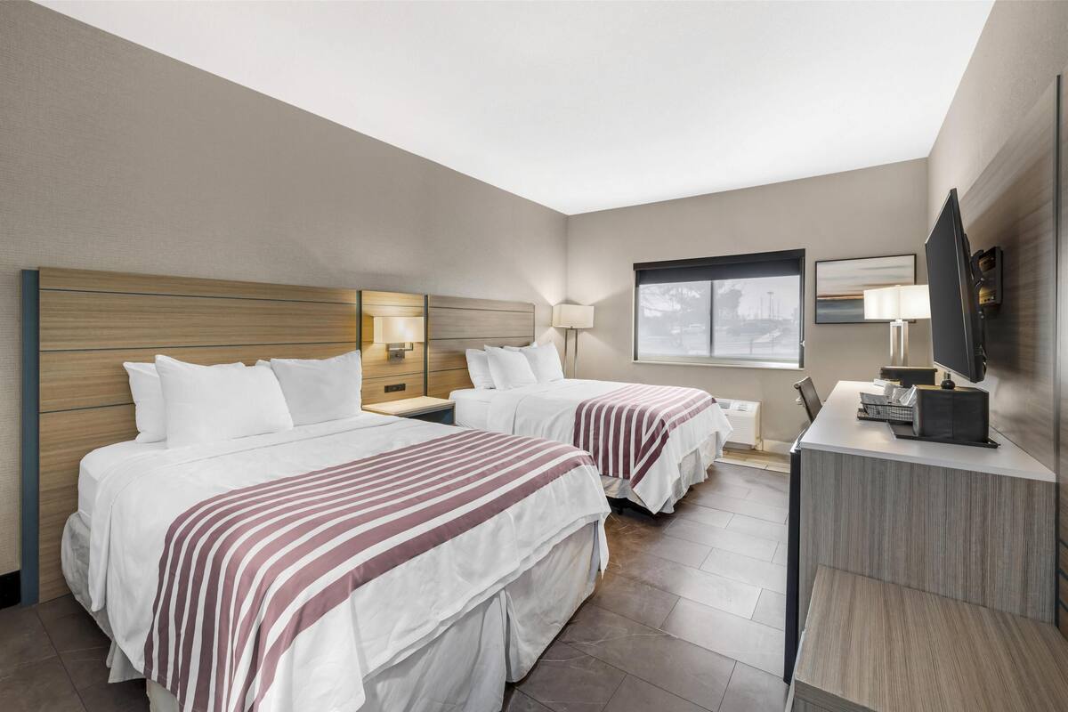 Ein Hotelzimmer mit zwei Betten, einem Schreibtisch, einem Fernseher und einem Fenster.