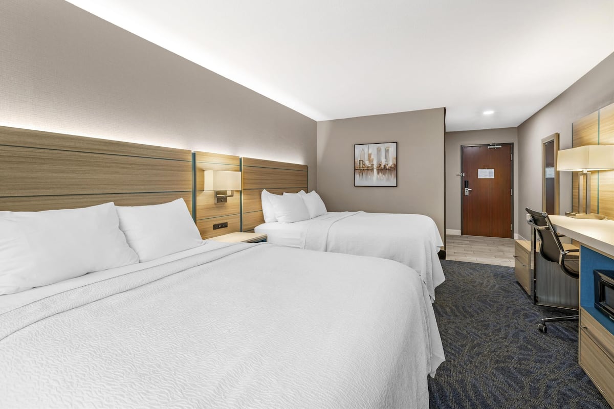 Ein Hotelzimmer mit zwei Betten, einem Schreibtisch, einem Stuhl, einer Lampe und einer Tür.