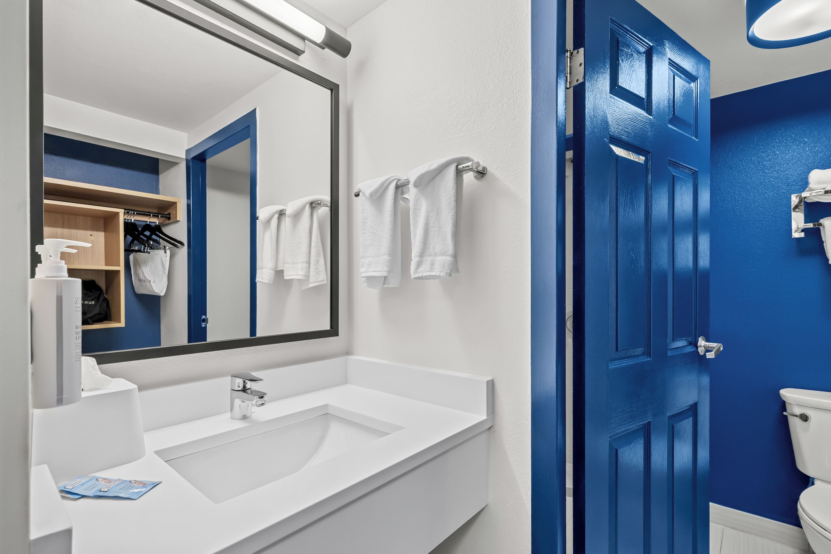 Une salle de bain avec un lavabo blanc, un grand miroir et une porte bleue.