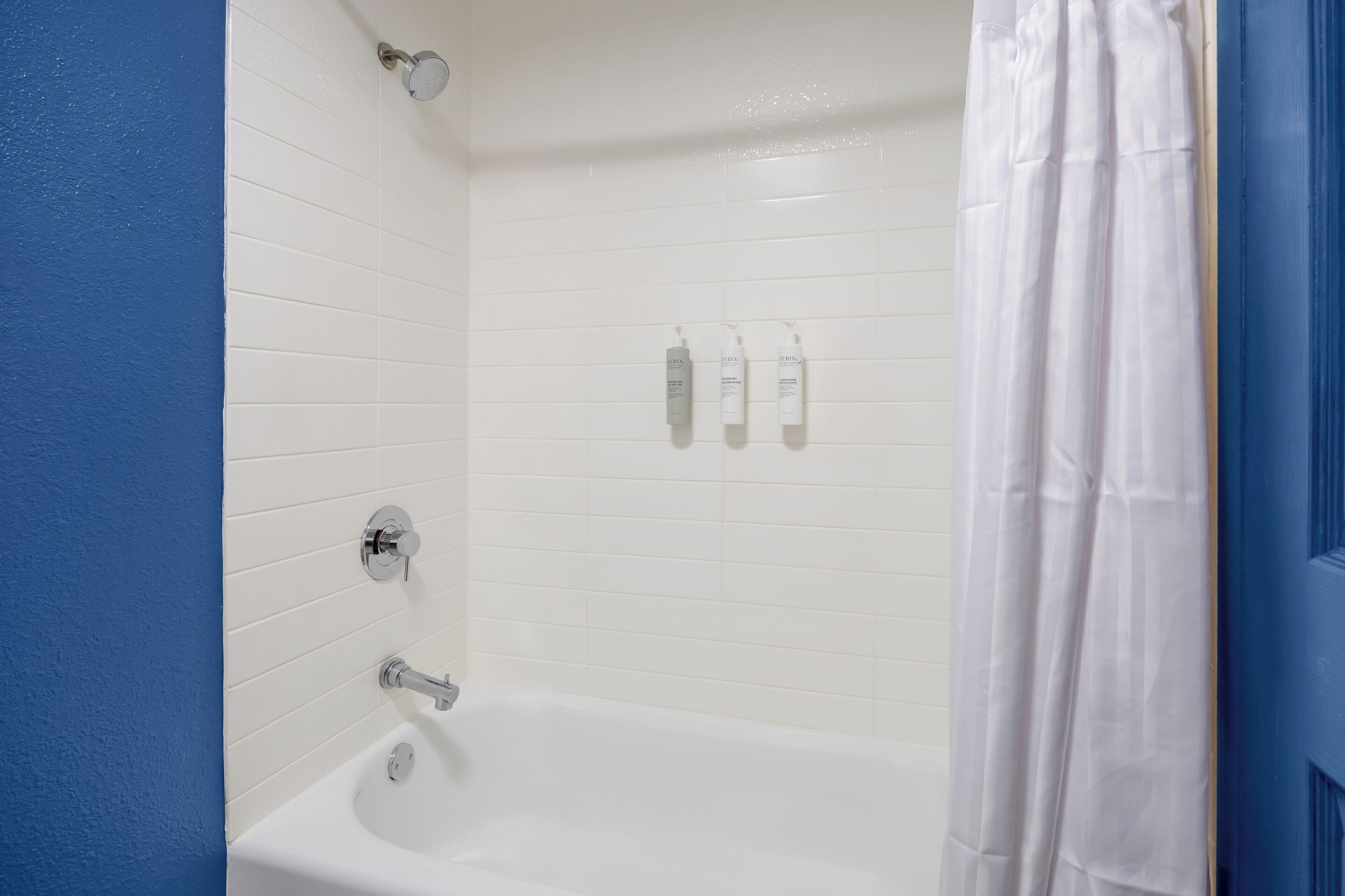 Een badkamer met een witte badkuip, een douchegordijn en drie toiletartikelen aan de muur.
