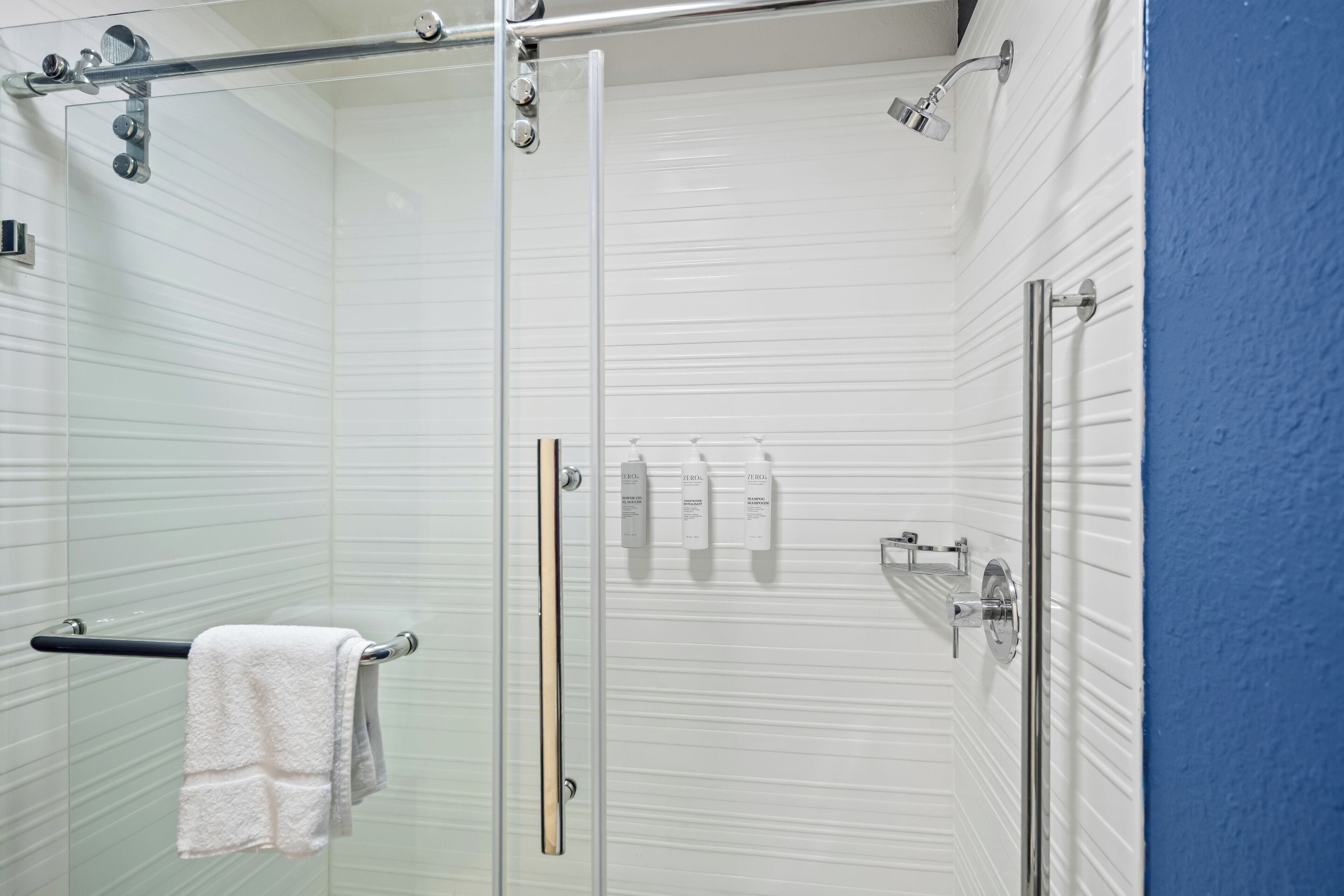 A glass-enclosed shower with a towel rack and toiletries.