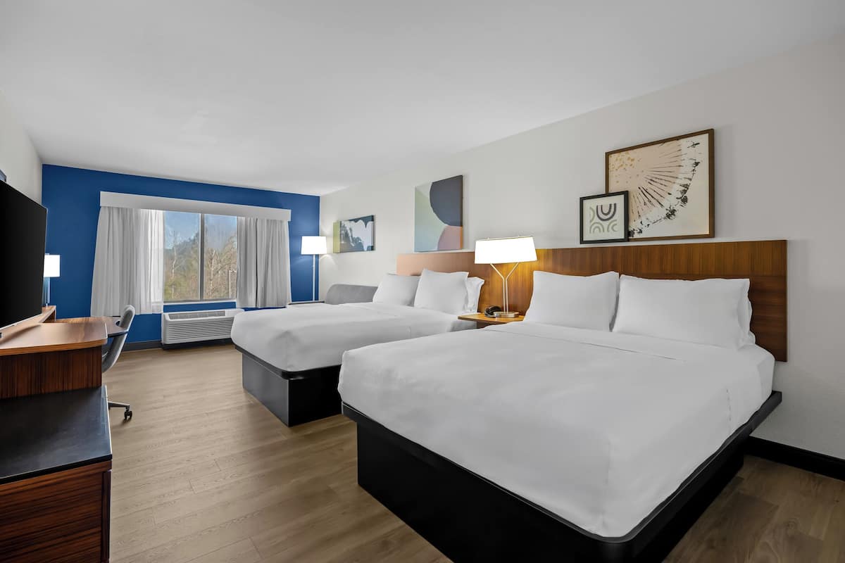 A hotel room with two beds, a desk, and a large window.