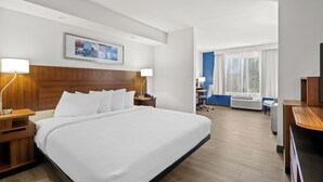 A hotel room with a large bed, wooden headboard, bedside tables with lamps, a desk with a chair, and a large window with curtains. - Spark by Hilton Macon North (Macon)