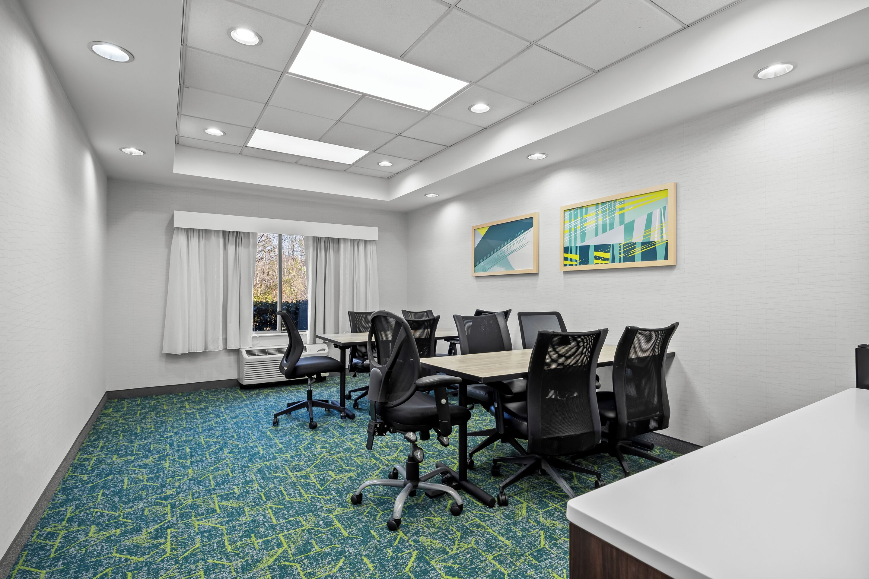 A conference room with a long table, black chairs, a whiteboard, and a window with curtains.