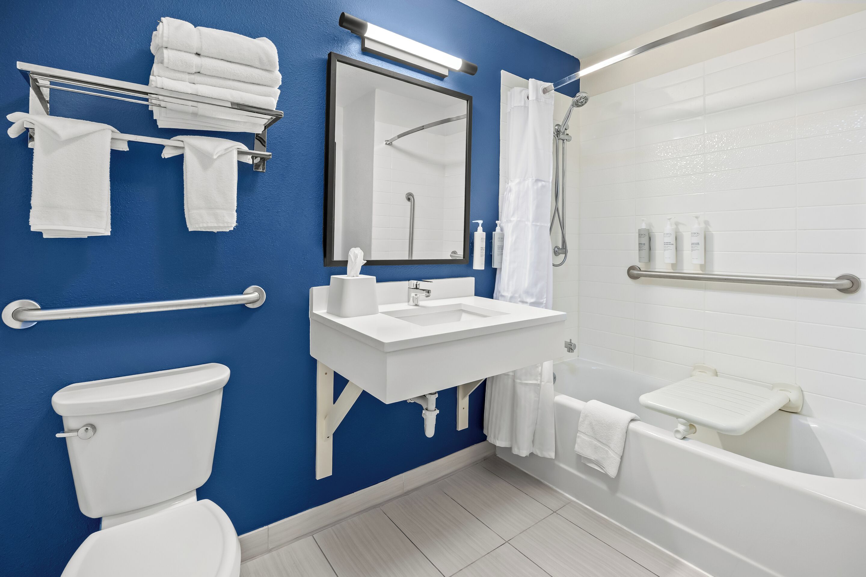 Ein modernes Badezimmer mit blauer Wand, weißen Armaturen, Toilette, Waschbecken, Badewanne, Dusche und einem Handtuchhalter.