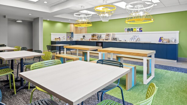 A modern cafe with multiple tables and chairs, a counter with a menu, and unique yellow pendant lights. - Spark by Hilton Macon North (Macon)