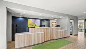 A modern hotel reception area with a wooden reception desk, a green rug, and a large abstract painting on the wall. - Spark by Hilton Macon North (Macon)