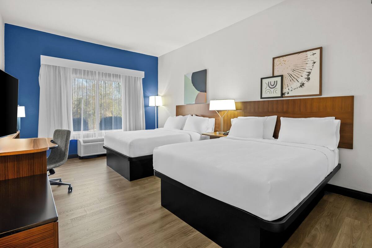 A hotel room with two beds, a desk, a chair, and a TV.