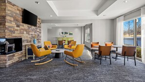 A modern lounge area with a stone wall, flat-screen TV, yellow chairs, and a dining table. - Spark by Hilton Macon North (Macon)
