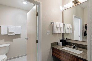 A bathroom with a toilet, a sink, and a mirror. There are towels hanging on a rack.