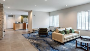 Een moderne hotellobby met een receptiebalie, een zithoek en een groot raam met gordijnen.
