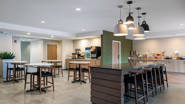 Een moderne keuken met een centraal eiland, barstoelen, hanglampen en diverse apparaten.
