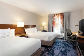 A hotel room with two beds, a desk with a TV, a chair, and a window with curtains.