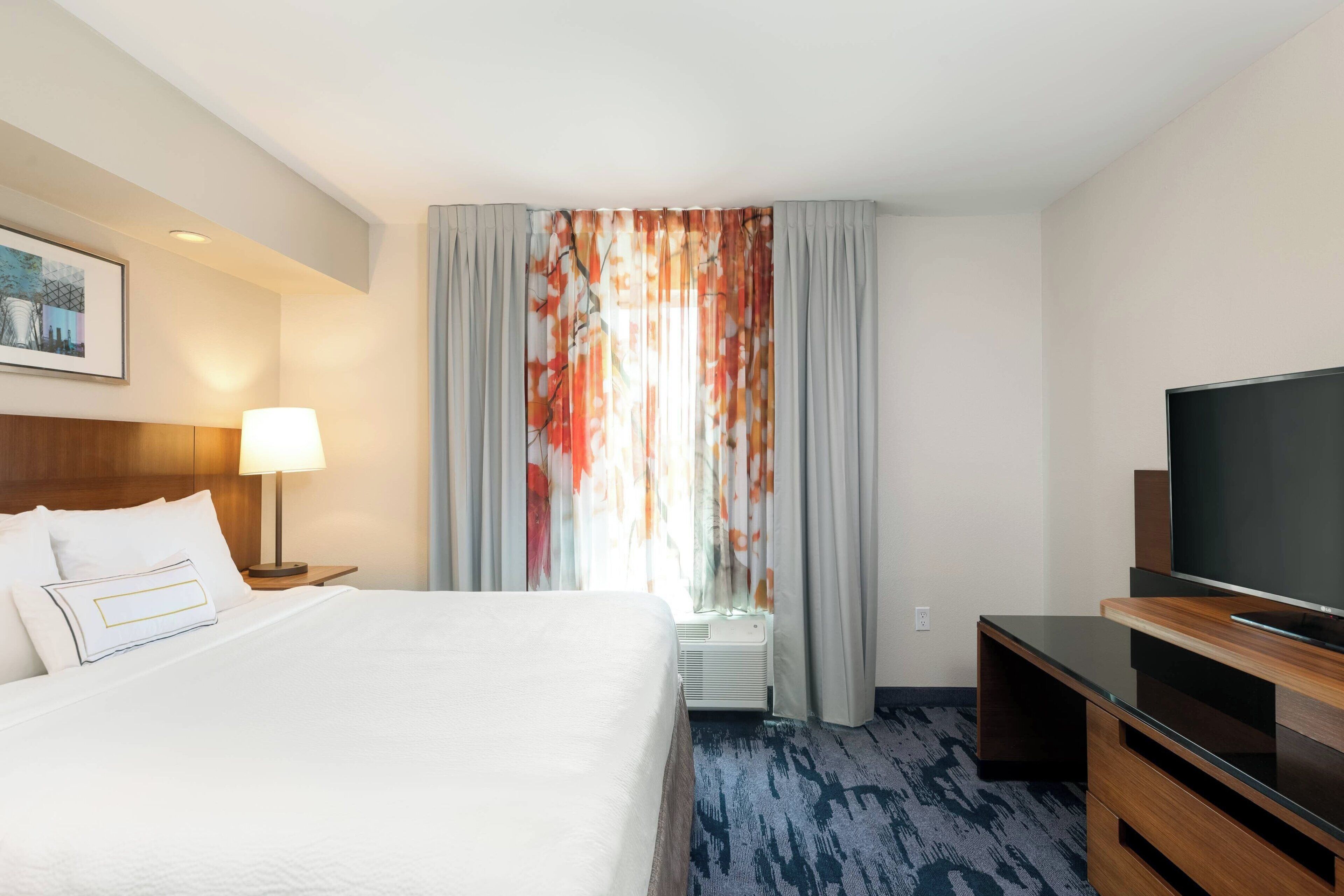 A hotel room with a bed, a TV, a lamp, and a window with curtains.