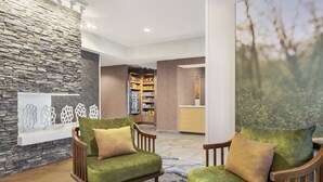 A lobby with two green armchairs, a white table, a stone wall, and a bookshelf in the background. - Fairfield Inn by Marriott Tracy (Tracy)