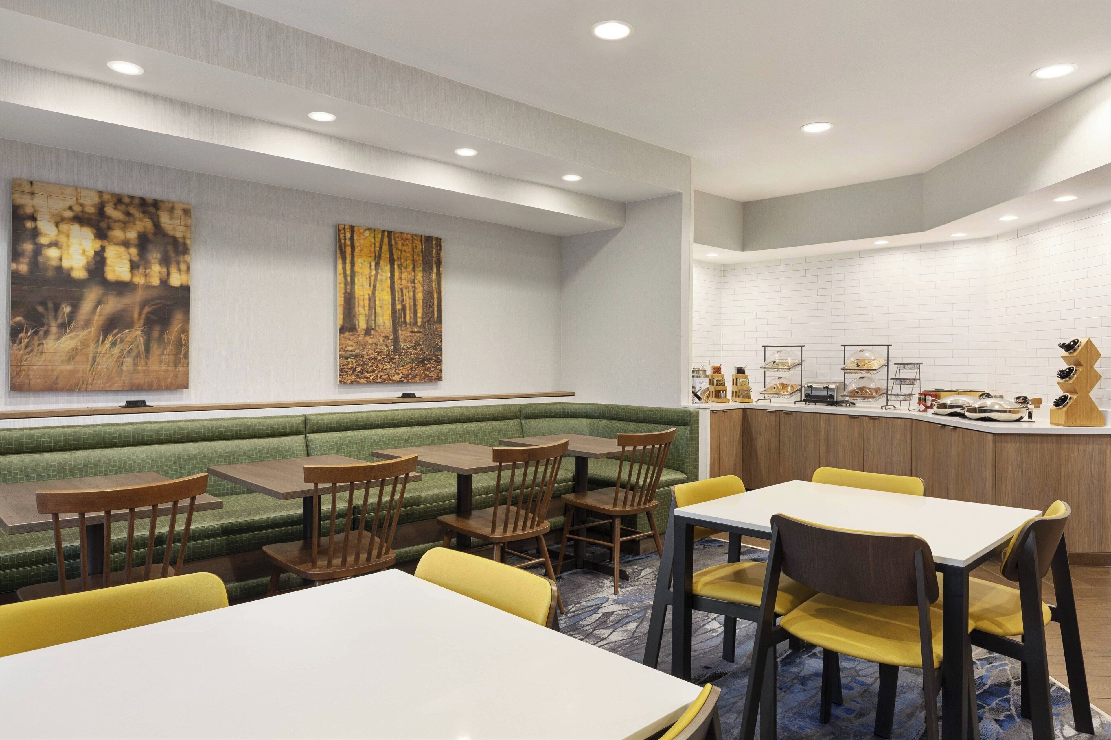 Comedor moderno con una banca tapizada de verde, mesas de madera y sillas amarillas.