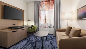 A hotel room with a flat-screen TV mounted on the wall, a desk with a chair, a sofa, a small table, and a window with curtains. - Fairfield Inn by Marriott Tracy (Tracy)