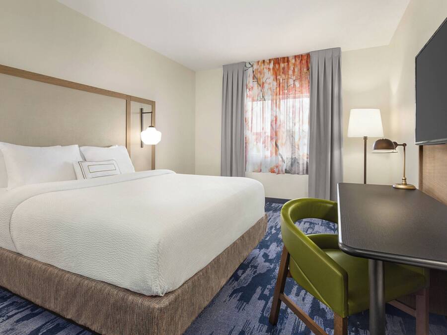 A hotel room with a large bed, a desk, a chair, a TV, and a window with curtains.