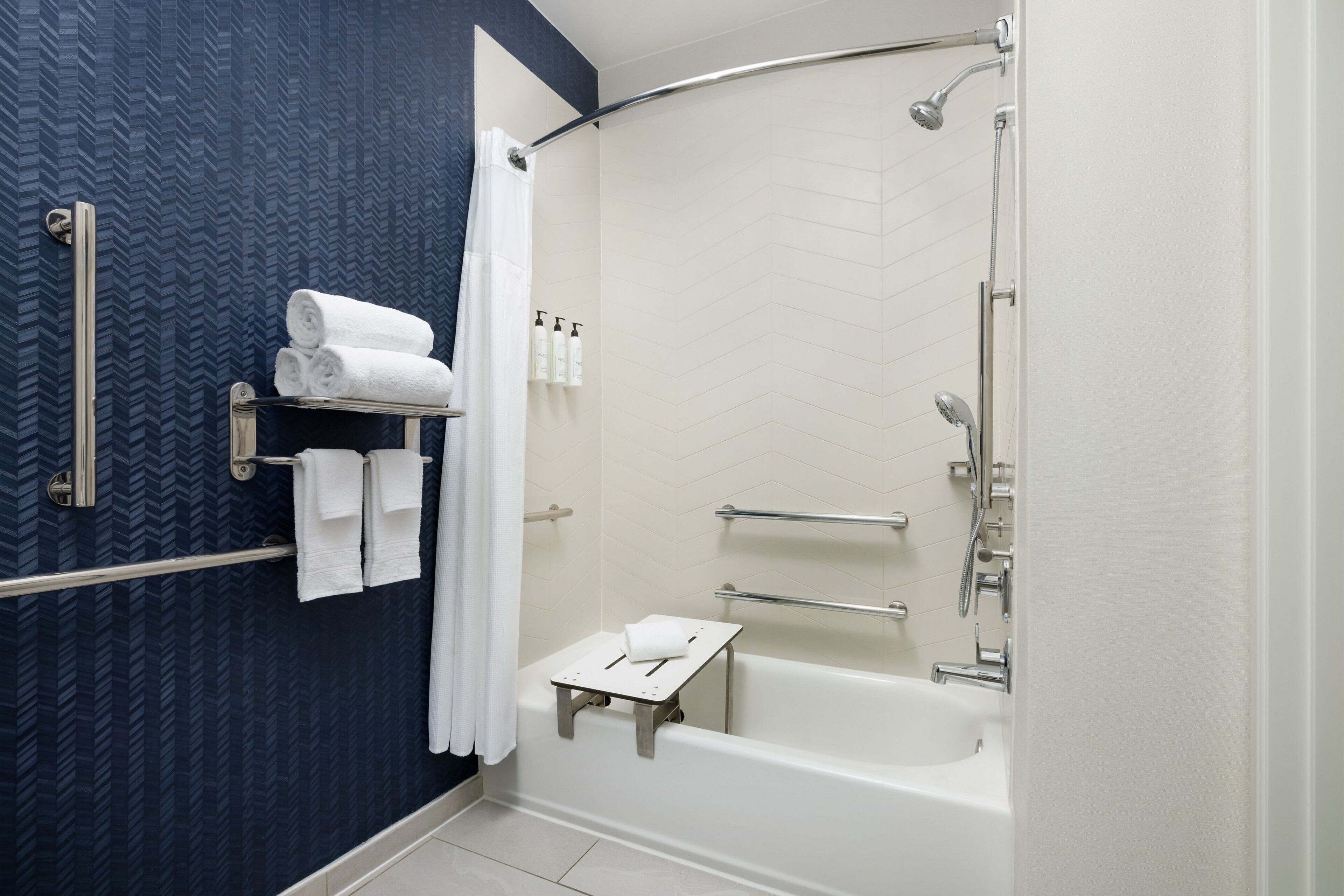 Een moderne badkamer met een gebogen douche, een witte badkuip en een handdoekrek met netjes gevouwen handdoeken.