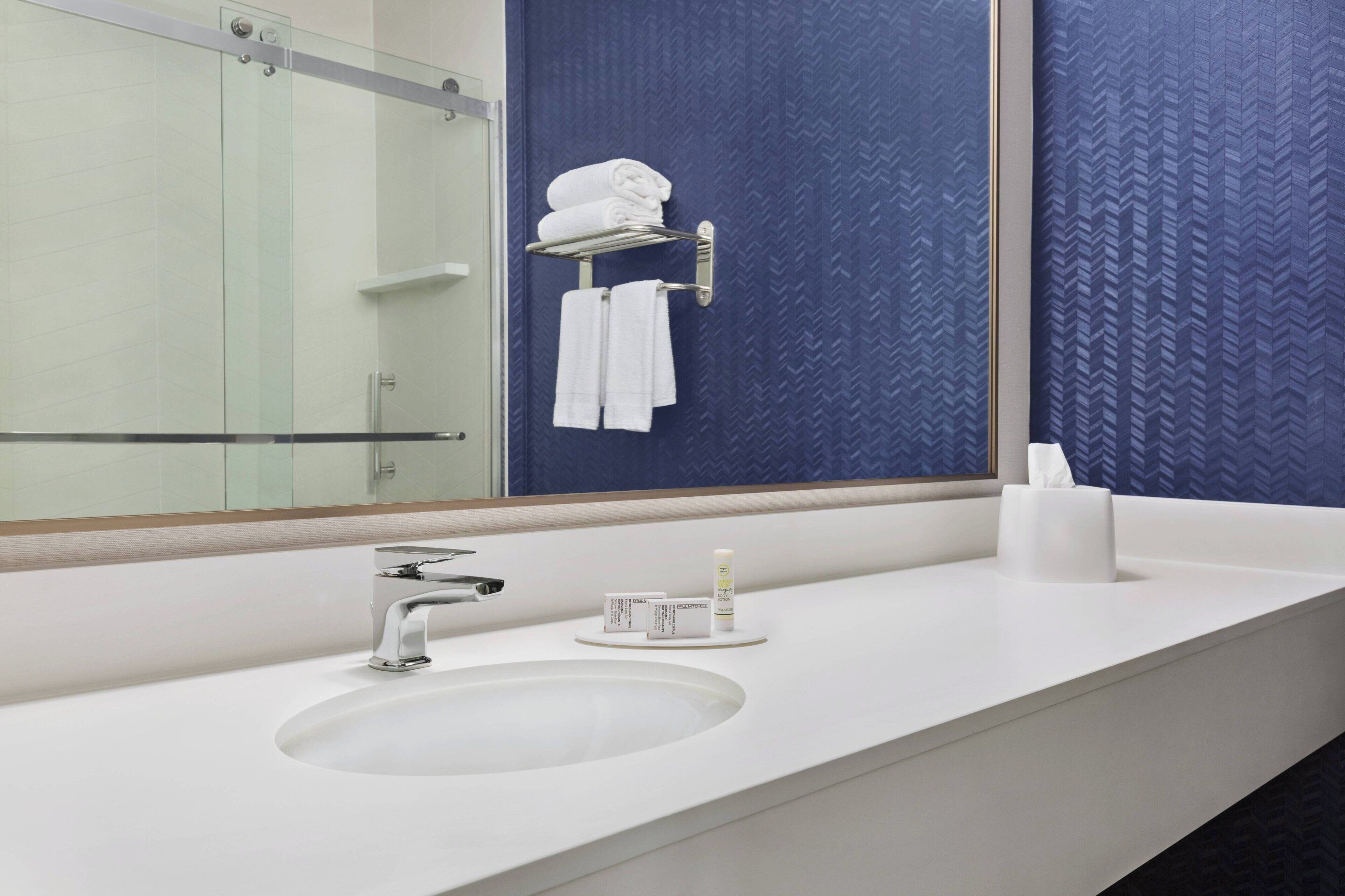 A modern bathroom with a large mirror, a white sink, and a towel rack with folded towels.