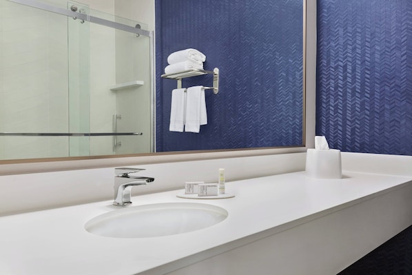 Une salle de bain moderne avec un grand miroir, un lavabo blanc et un porte-serviettes où sont pliés des serviettes.