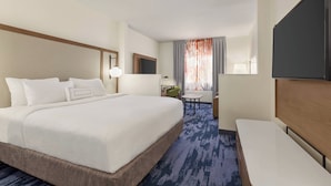 A hotel room with a large bed, a desk, a chair, a TV, and a window with curtains. - Fairfield Inn by Marriott Tracy (Tracy)