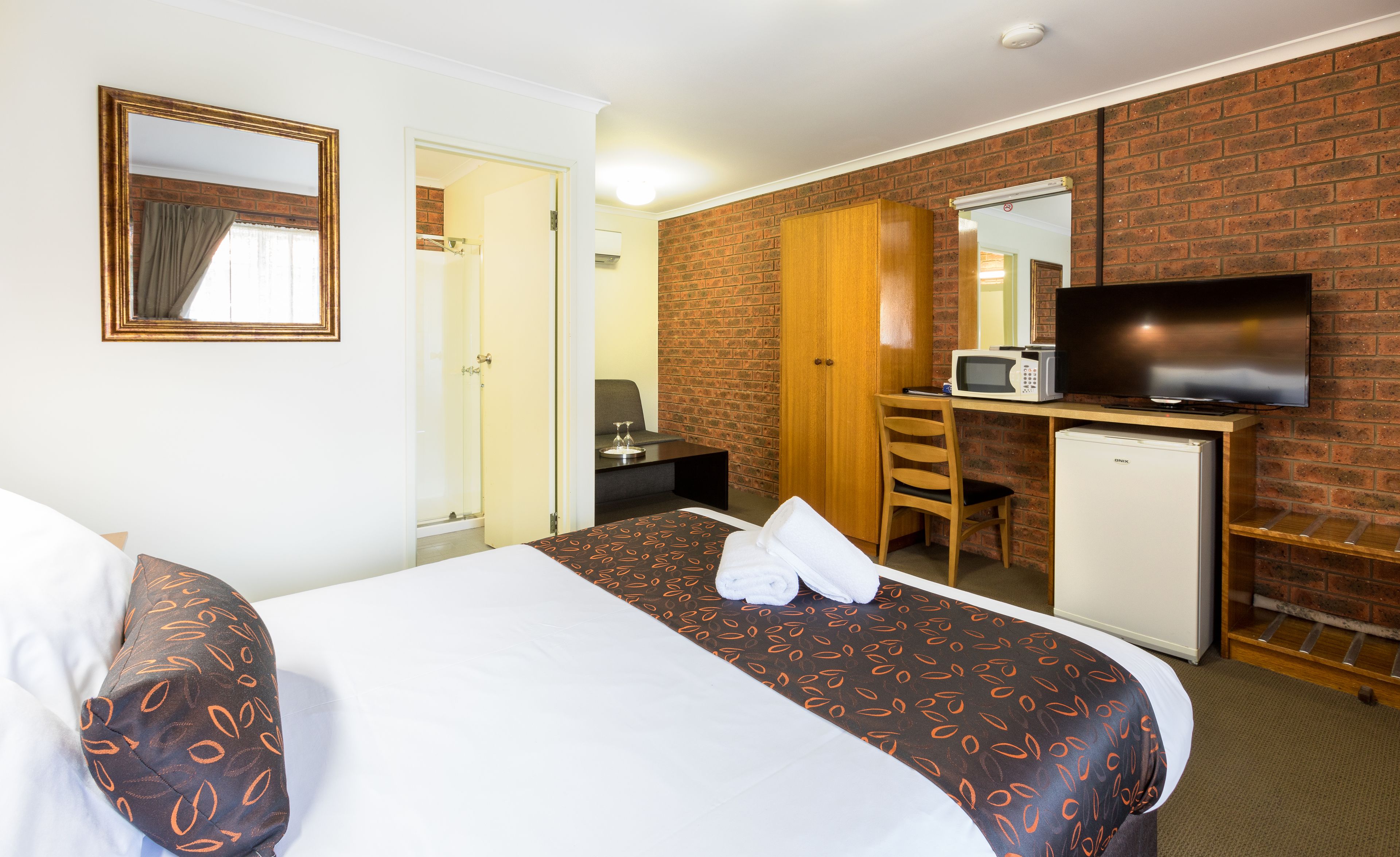 A hotel room with a bed, a desk, a television, and a microwave.