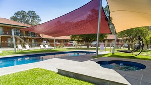 Una piscina con sombrilla, sillas de descanso y un pequeño jacuzzi.