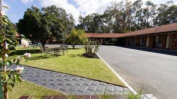 A motel with a paved driveway, a lawn with a table and chairs, and a row of rooms with a red roof.
