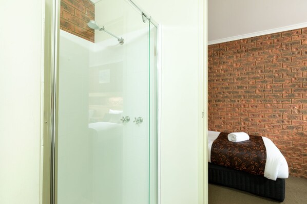A room with a glass shower enclosure, a brick wall, and a bed with a patterned bedspread. - Advance Motel (Wangaratta)