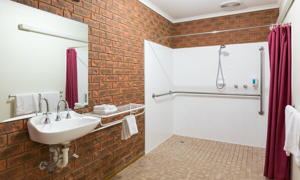 Une salle de bain avec un lavabo blanc, un miroir, une douche équipée d’une barre d’appui et un rideau rouge.