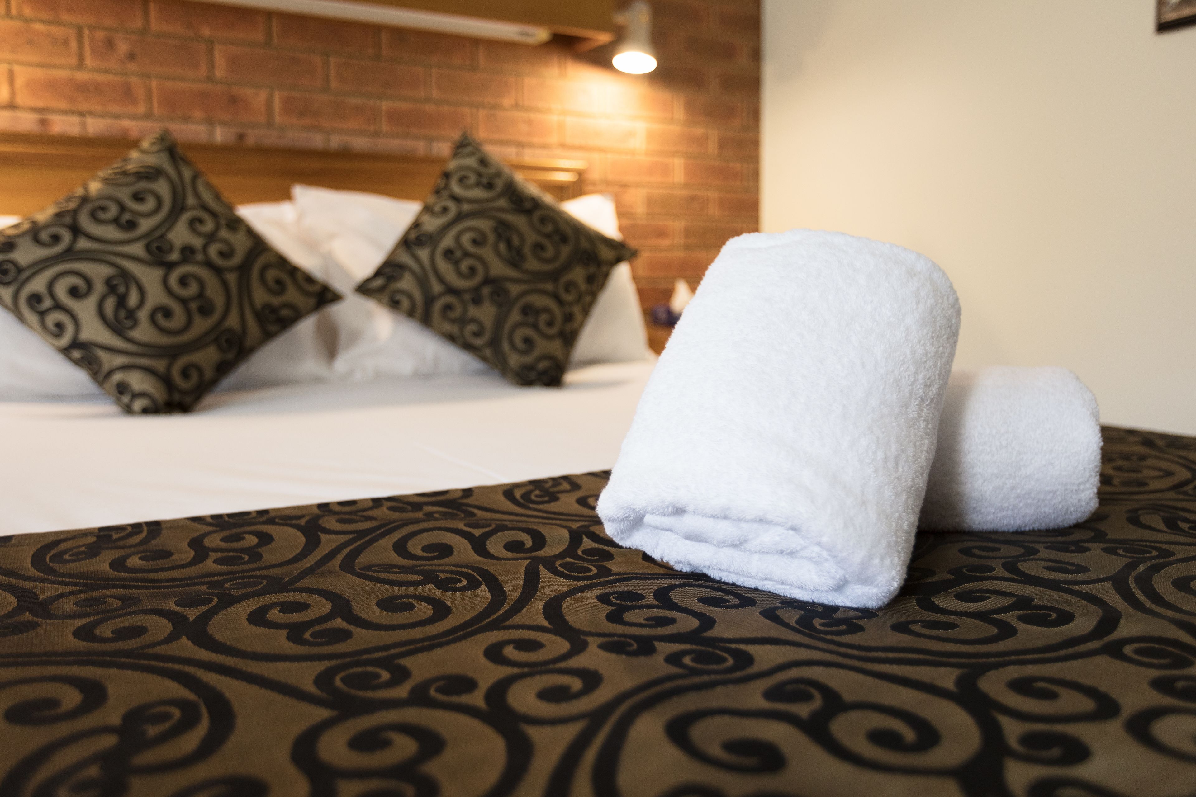 Una cama bien hecha con almohadillas estampadas y una toalla blanca doblada sobre una colcha estampada.