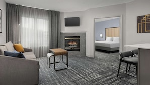 A modern hotel room with a fireplace, a sofa, a dining area, and a bed.