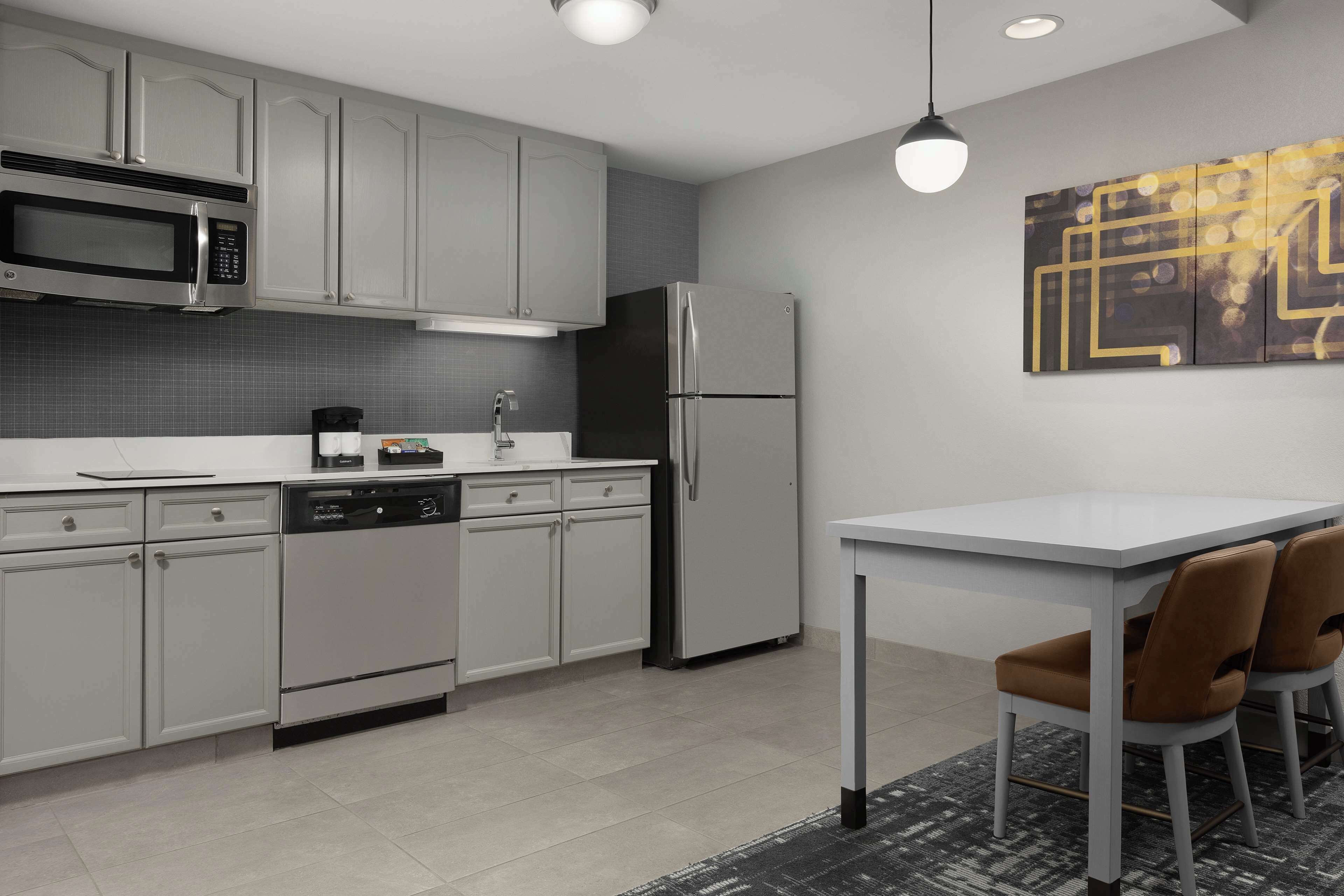 A modern kitchen with stainless steel appliances, grey cabinets, and a dining area with a white table and brown chairs.