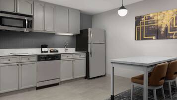 A modern kitchen with stainless steel appliances, grey cabinets, and a dining area with a white table and brown chairs.
