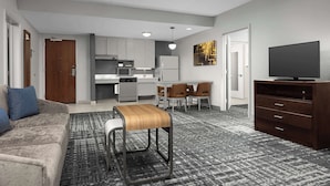 A modern living room with a sofa, a coffee table, a TV stand, and a kitchen area in the background.
