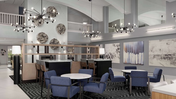 A modern hotel lobby with a central seating area, a staircase, and artwork on the walls.