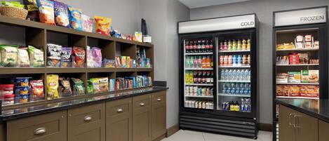 A kitchenette with shelves stocked with snacks and a refrigerator with a 'COLD' and 'FROZEN' section.