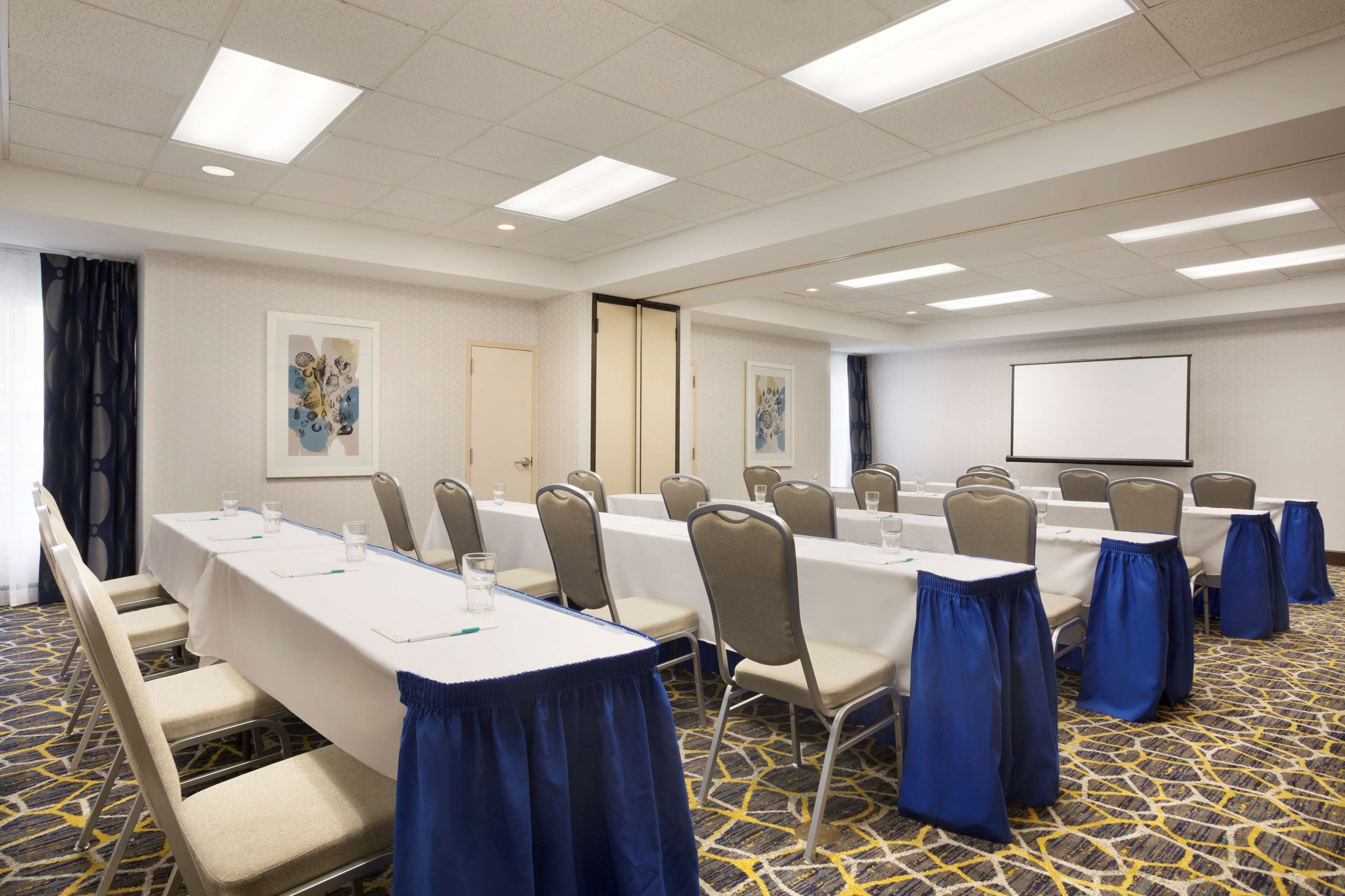 A conference room with long tables, chairs, and a projector screen.