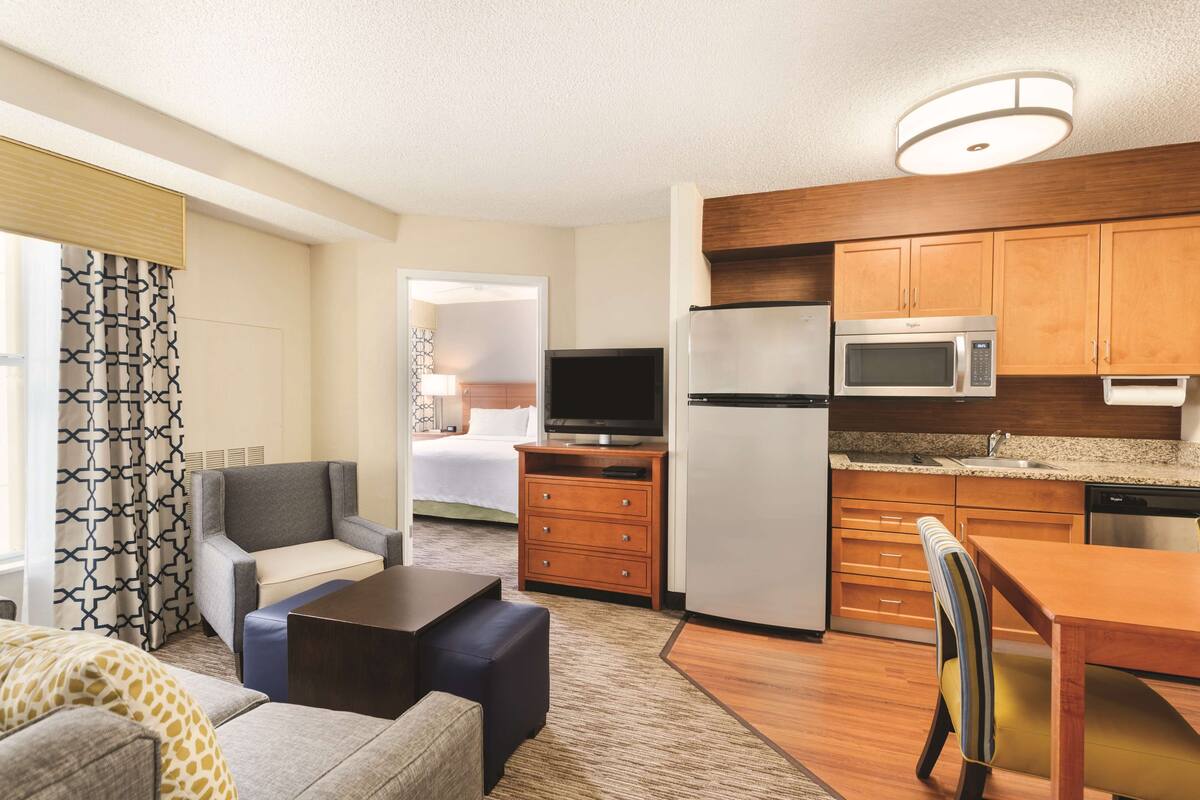A compact hotel room with a kitchenette, a sofa, a coffee table, a TV, and a bed.