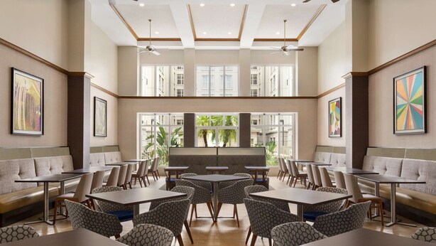 A spacious dining area with high ceilings, multiple seating options including tables and booths, and large windows providing natural light.