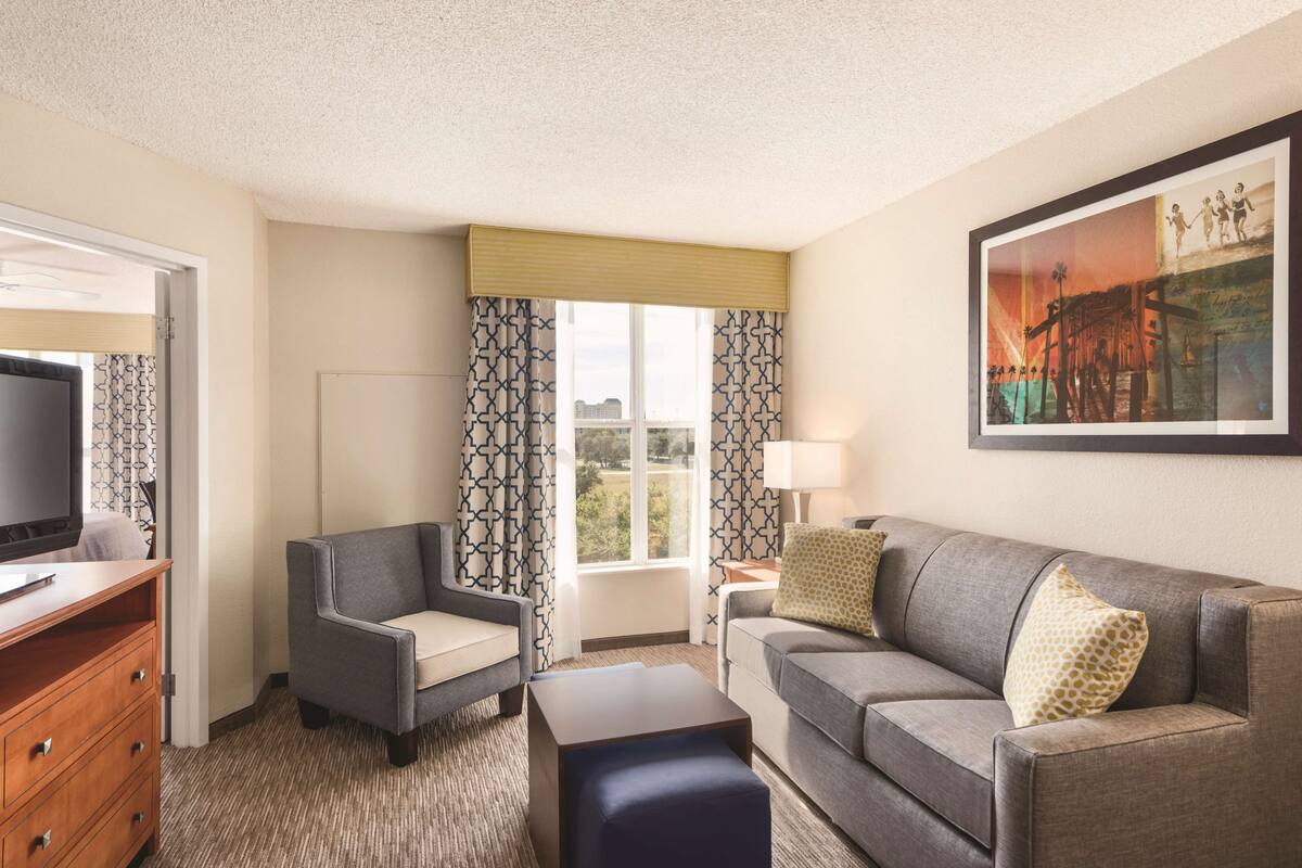 A hotel room with a sofa, two armchairs, a TV, a lamp, and a painting on the wall.