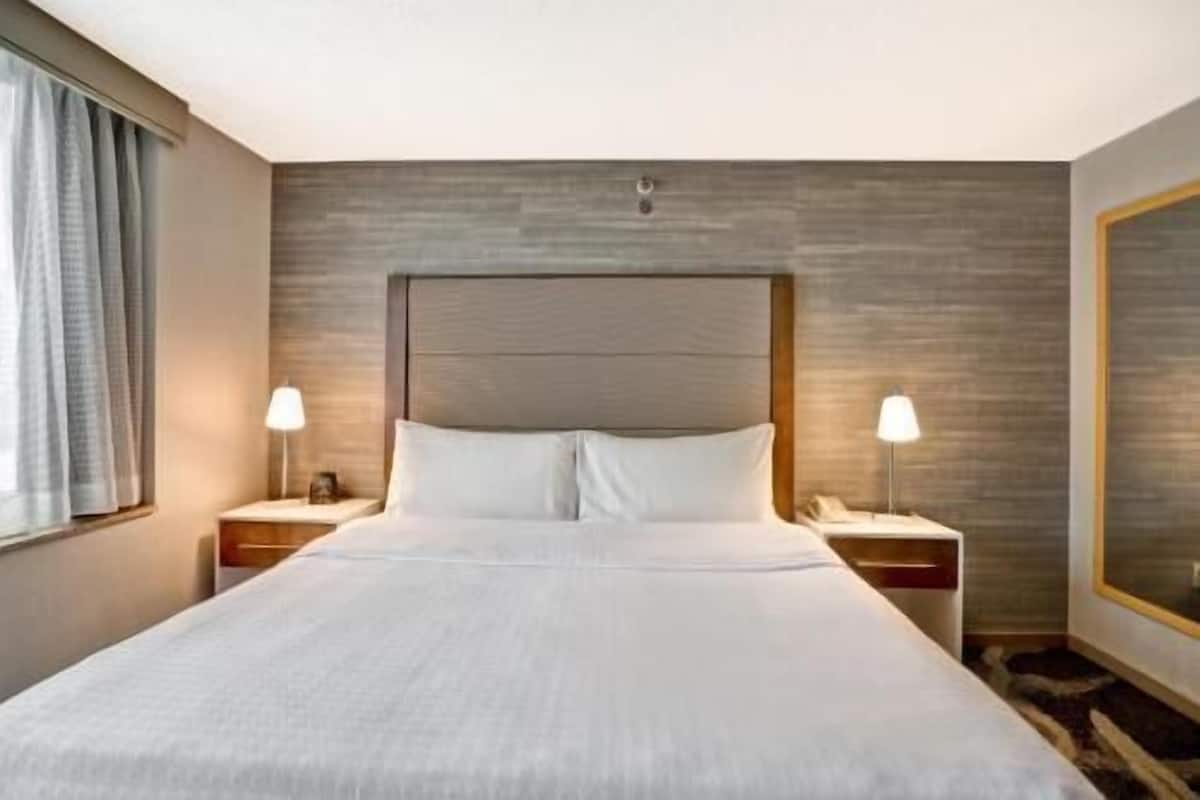 Hotellihuone, jossa on suuri sänky, kaksi yöpöytää valaisimineen, sängynpääty ja suuri peili.