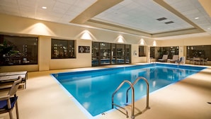 Une piscine intérieure à l’eau claire, entourée de chaises longues et dotée d’un mur en verre.