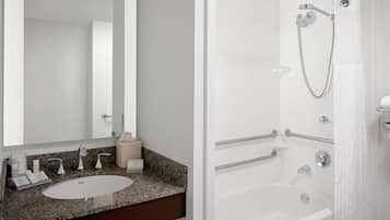 A modern bathroom with a granite countertop, a large mirror, a sink, and a walk-in shower with grab bars.