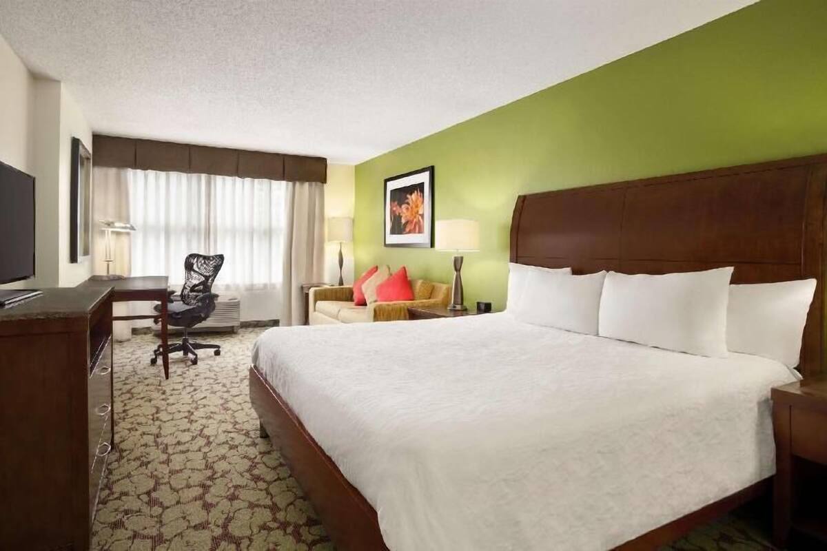 A hotel room with a large bed, a desk, a chair, and a television.