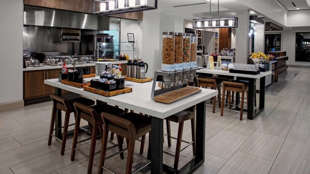 A modern kitchen with a central island, bar stools, and a coffee station. - Hilton Garden Inn Atlanta Perimeter Center (Atlanta)