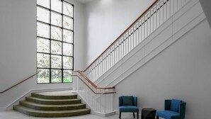 A staircase with white railings and wooden handrails, leading to a landing with two blue chairs and a small black table. - Hilton Garden Inn Atlanta Perimeter Center (Atlanta)