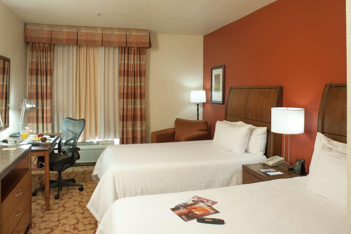 A hotel room with two beds, a desk with a chair, a lamp, and a telephone.