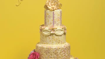 Un gâteau à plusieurs étages, décoré de motifs floraux et orné d’un ruban, le tout sur un fond jaune.
